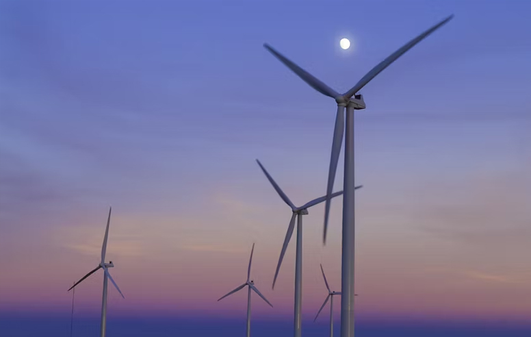 Wind turbines at dusk with a soft purple and orange sky and the moon glowing above the horizon.